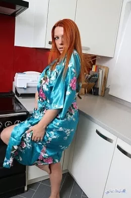 Kate Star at Satin Silk Fun | We come across redhead Kate Star in the kitchen. She is wearing a wrap around shiny blue patterned satin  gown. Of course, it is only kept secure by a small, flimsy little satin belt that is barely holding it together and from time to time reveals a little more of the lovely Kate