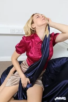 Poppy at Satin Silk Fun | Poppy is in her bedroom and she is wearing a red satin button up blouse and a long beige satin skirt.  You would of course like to see her enjoying the feel of the satin fabric as she rolls her hands over the royal blue satin sheets