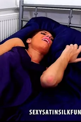 Jess West at Sexy Satin Silk Fun | Jess West is laying on her bed in her bedroom. She is wearing a dark blue / purple satin chemise and she looks more or less ready for be but she feels the soft fabric around her body and invites you come and take a much closer look